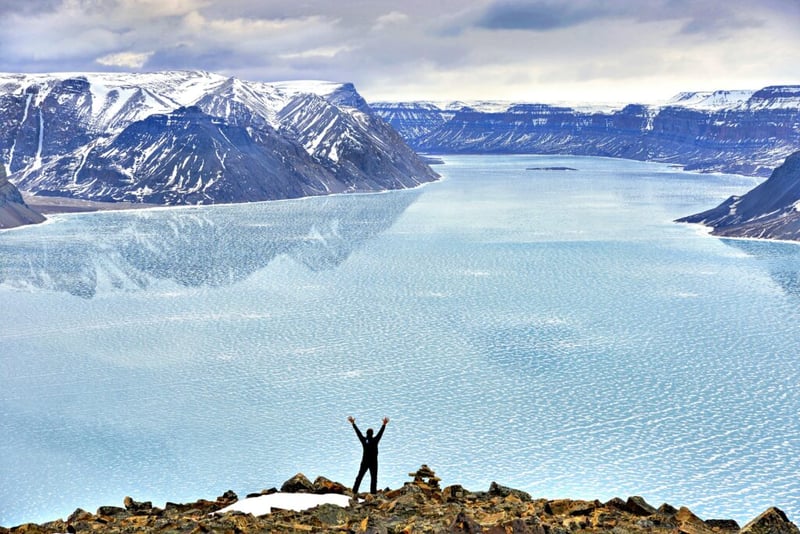 man stood in front of frozen lake with mountains in the background