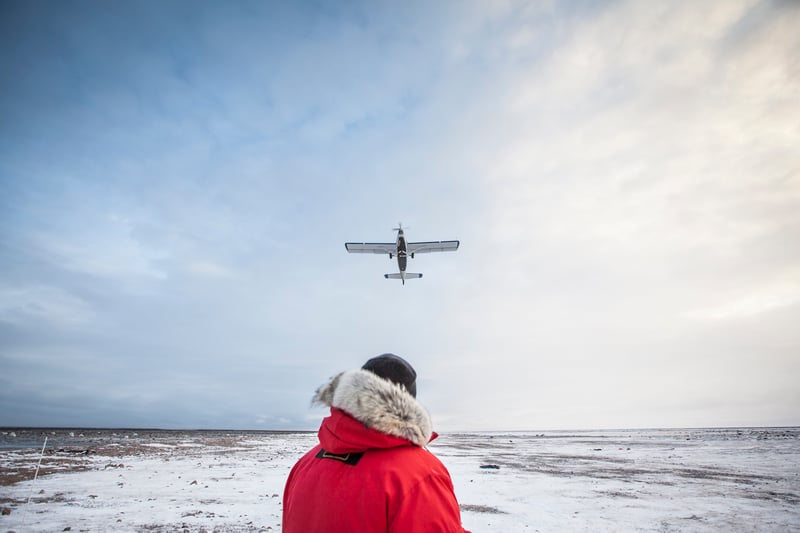 person surrounded by snow and ice looking into the sky with an aircraft above